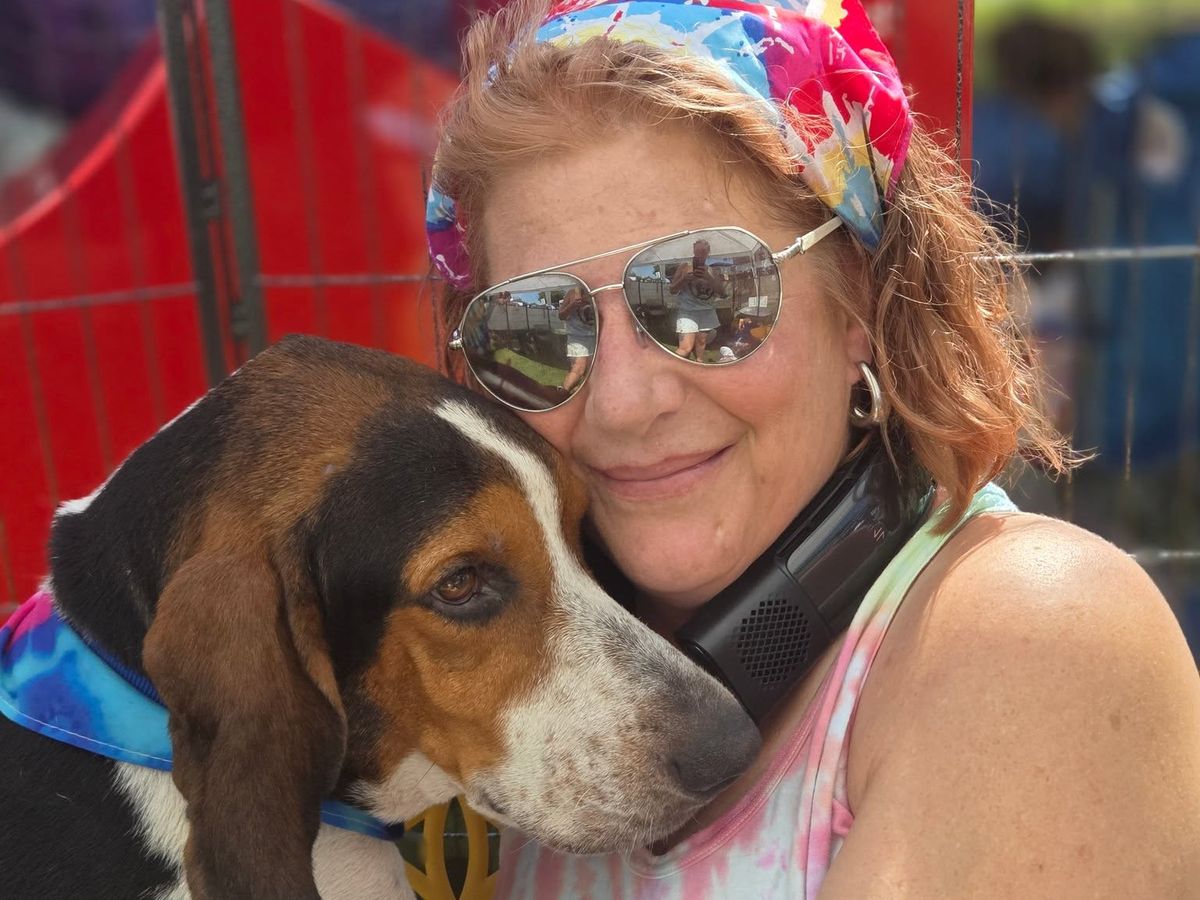 A volunteer in a Helpless Hounds shirt hugging a hound at an adoption event